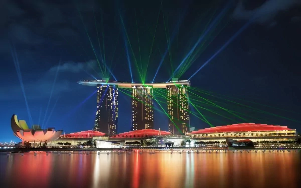 Nighttime view of Singapore's Marina Bay Sands with vibrant green laser lights illuminating the sky, reflected on calm waters in this HD desktop wallpaper.