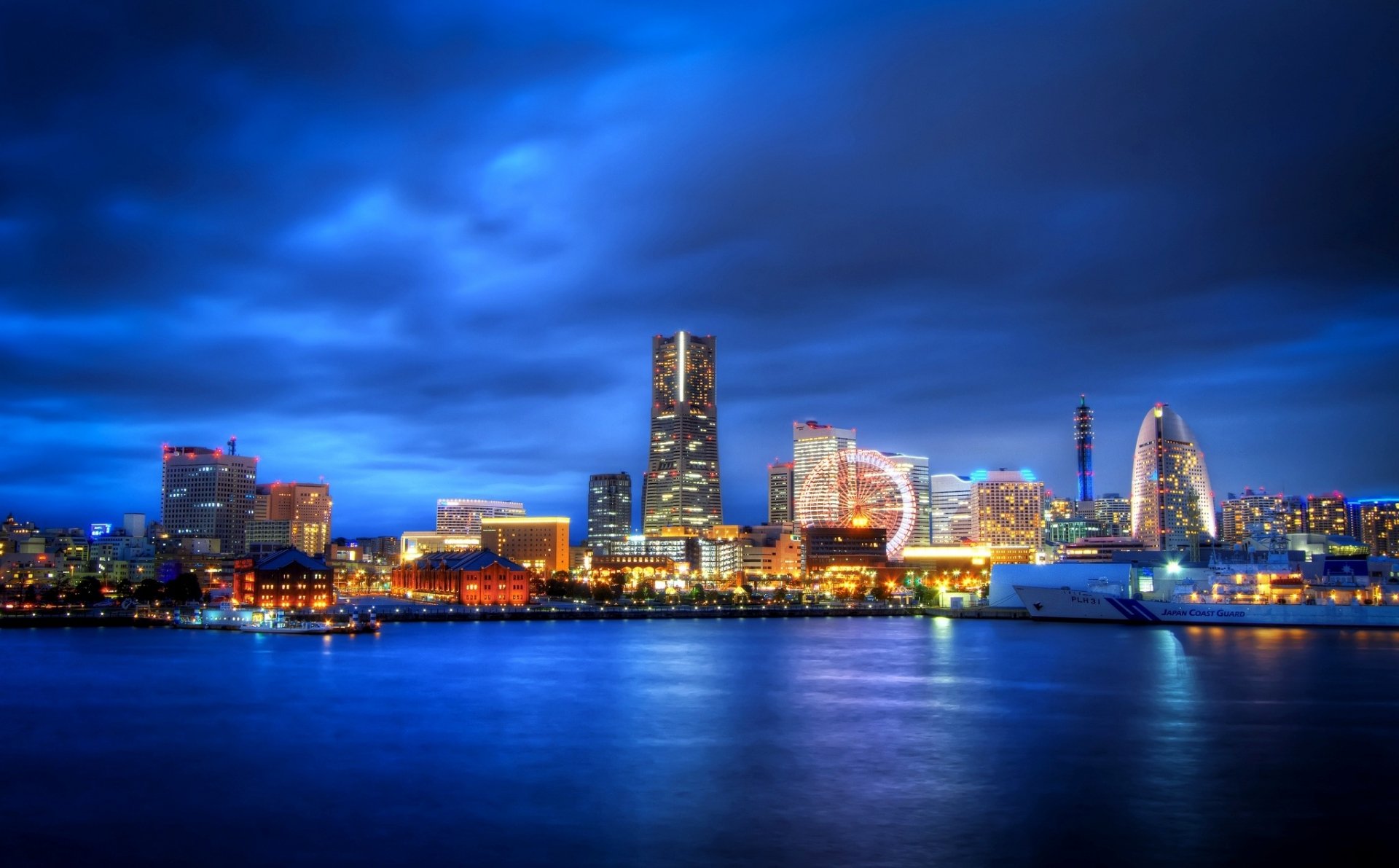 HD desktop wallpaper of Yokohama’s illuminated man-made skyline reflecting on calm waters under a dramatic blue evening sky.