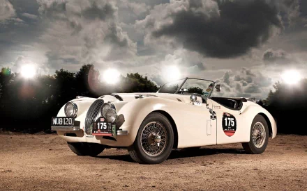 HD PC desktop wallpaper and background: white Jaguar XK120 roadster (#175) parked on dirt under a dramatic cloudy sky with bright studio lights.