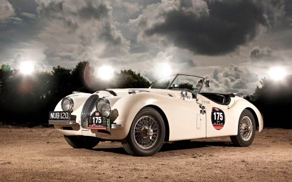 HD PC desktop wallpaper and background: white Jaguar XK120 roadster (#175) parked on dirt under a dramatic cloudy sky with bright studio lights.