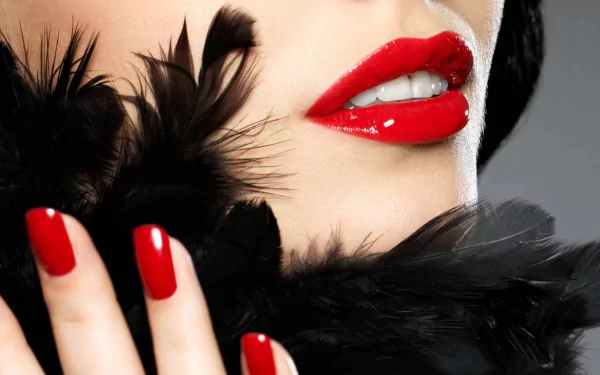 A striking HD desktop wallpaper featuring a close-up of a woman's lips adorned in bold red lipstick, complemented by perfectly manicured red nails and a touch of black feathers.
