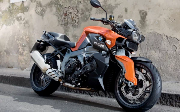 HD PC desktop wallpaper and background: orange-and-black BMW K1300R motorcycle parked by a weathered wall, close-up view of the vehicle.