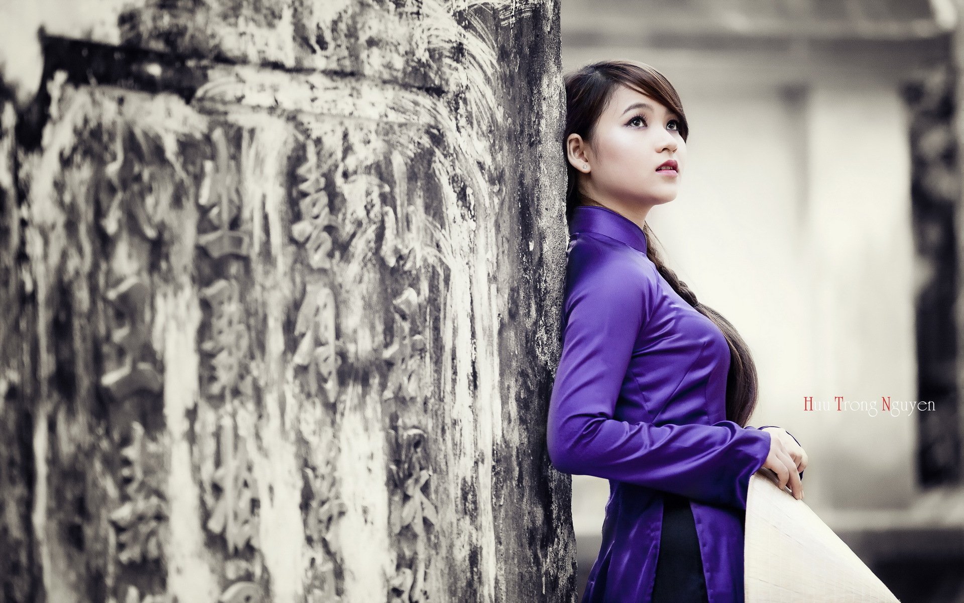 HD desktop wallpaper featuring an Asian woman in a purple dress, leaning against a stone wall with an intricate texture.