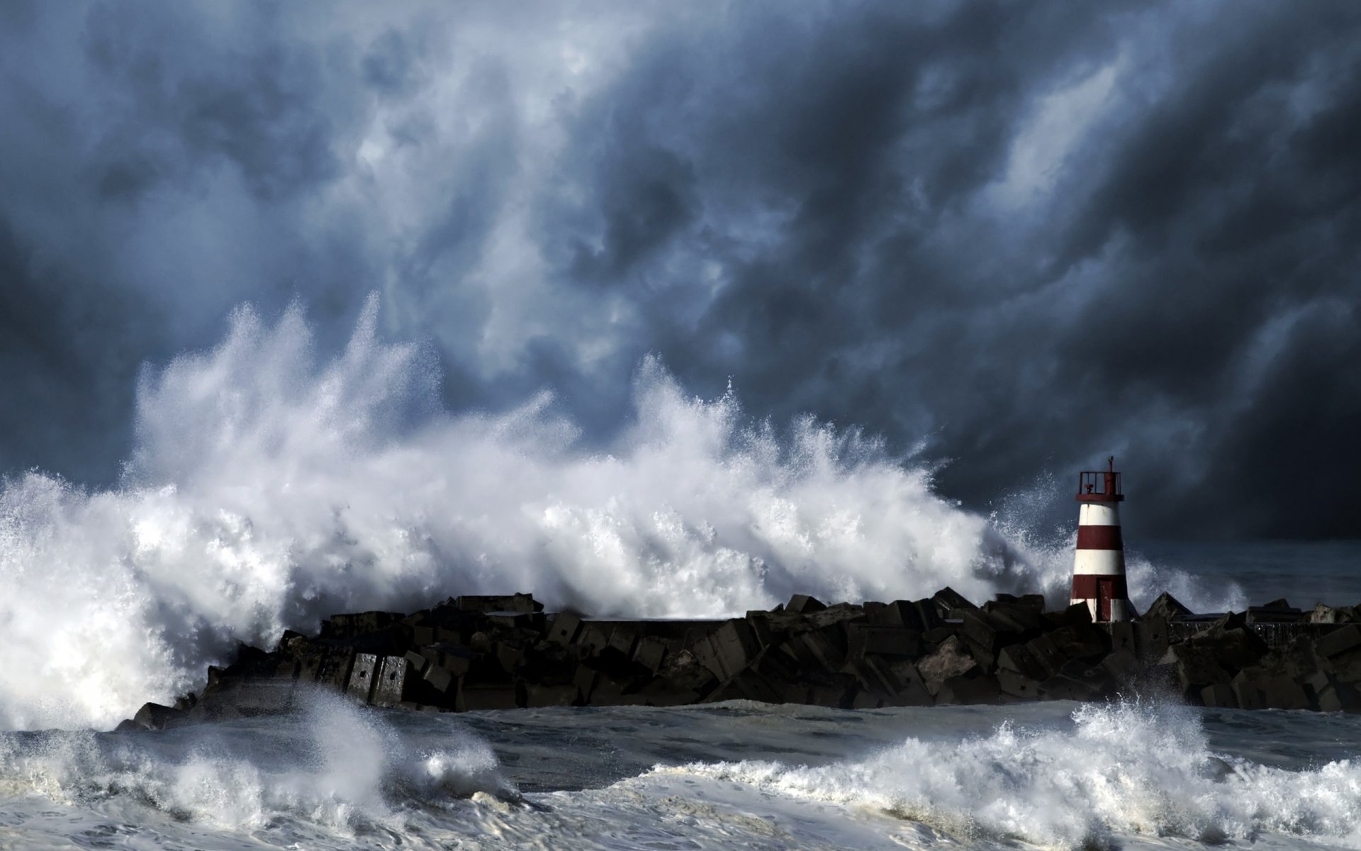 A dramatic scene featuring a lighthouse amidst crashing waves and dark stormy skies, showcasing the power of nature in this HD PC desktop wallpaper.