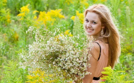 A smiling woman with long hair poses in a field of yellow and green foliage, holding a large bouquet of white flowers. The image exudes a summer mood and makes a vibrant HD desktop wallpaper background.