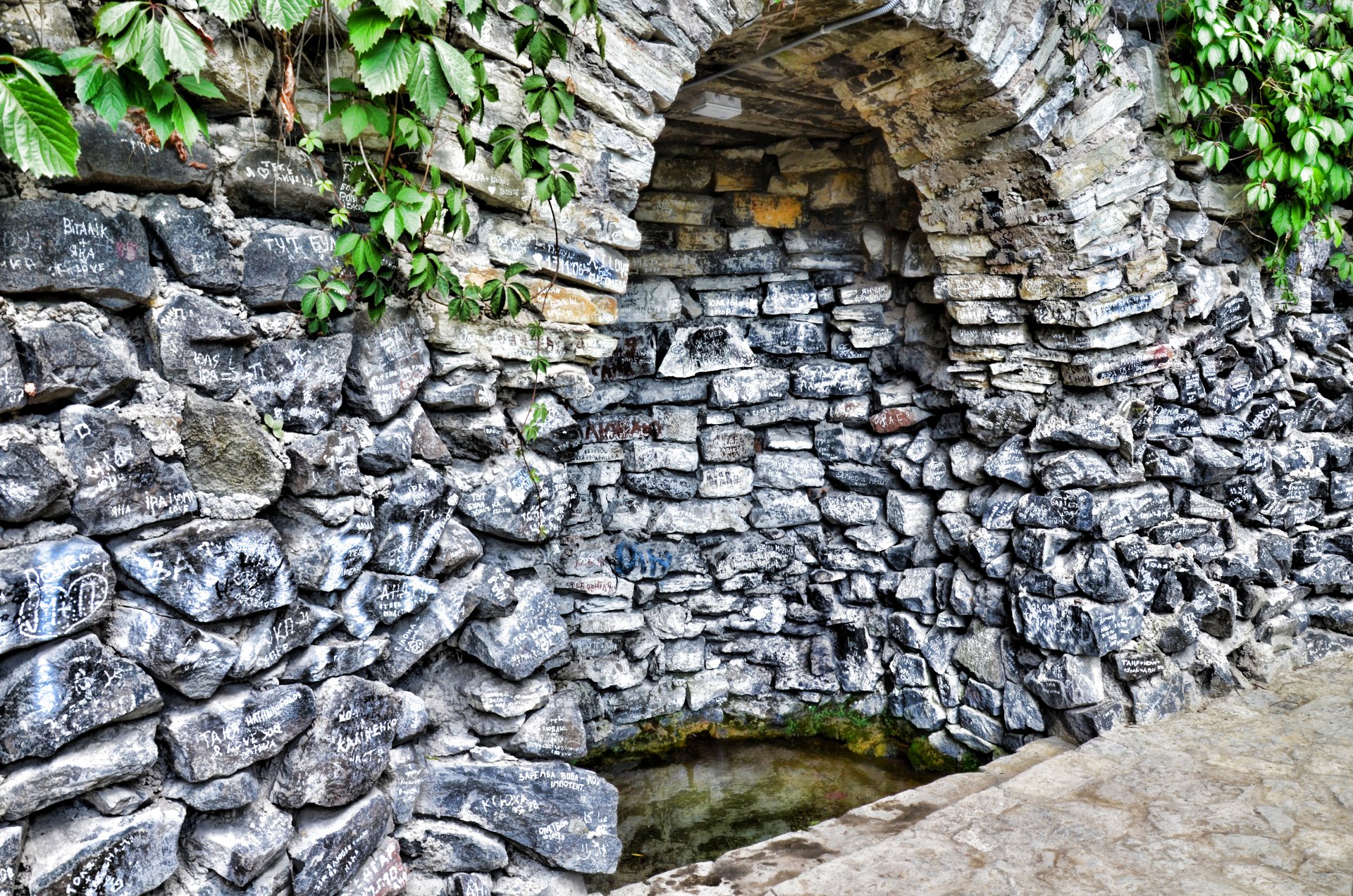 4K Ultra HD wallpaper showing a man-made stone tunnel with an arched entrance, surrounded by lush green foliage on a rugged stone wall.