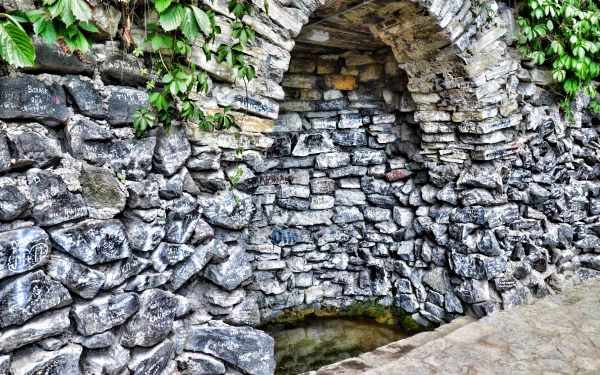 4K Ultra HD wallpaper showing a man-made stone tunnel with an arched entrance, surrounded by lush green foliage on a rugged stone wall.