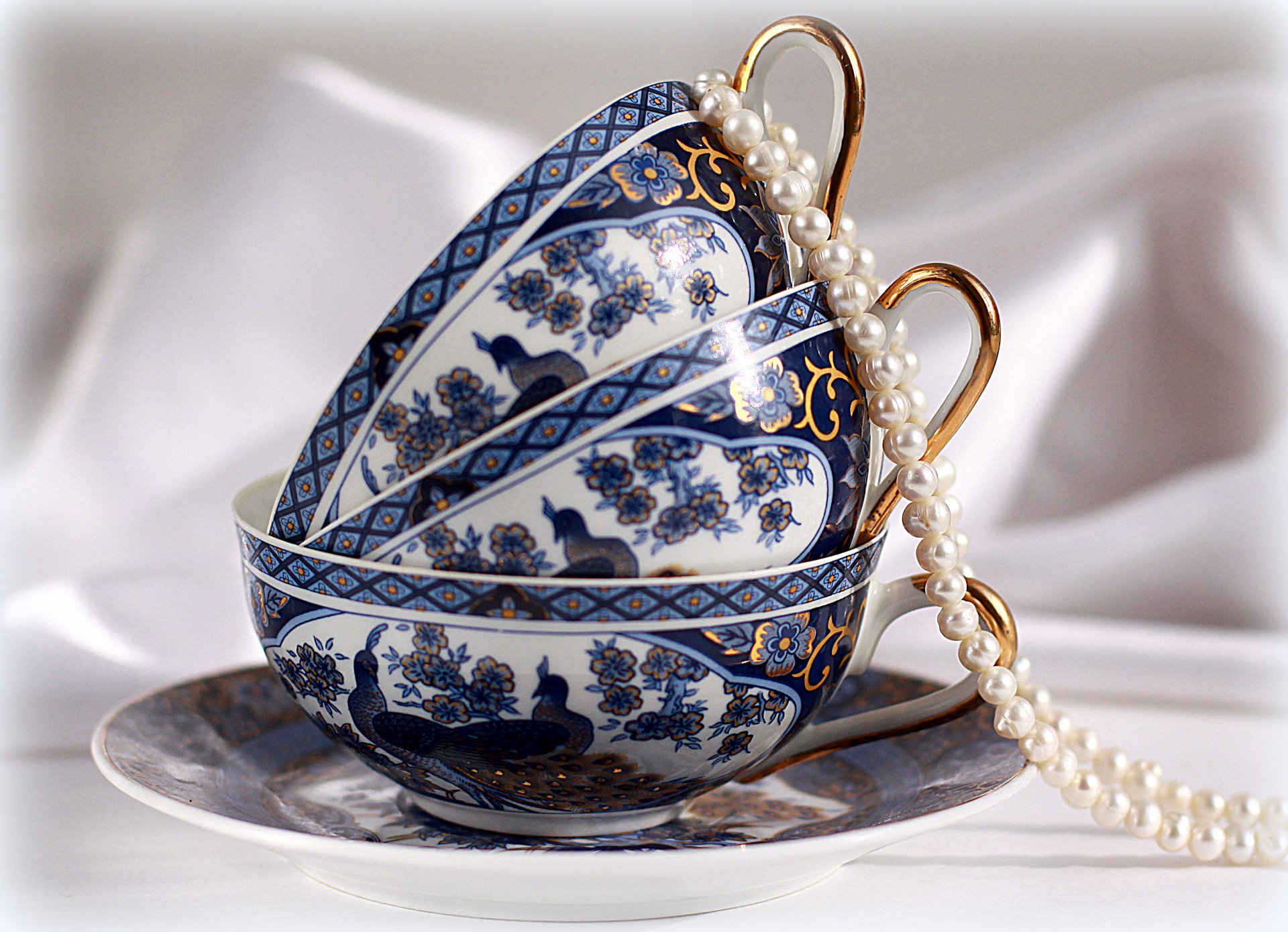A still life 4K Ultra HD desktop wallpaper featuring elegant stacked blue and white patterned cups with a strand of pearls draped over them, captured in fine photography.