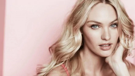 A captivating HD desktop wallpaper featuring a woman with long blonde hair and striking blue eyes against a soft pink background, showcasing elegant beauty and confidence.