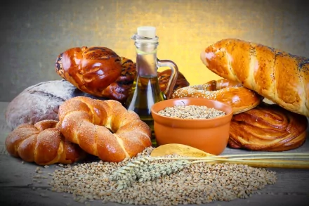 A vibrant HD wallpaper showcasing an assortment of freshly baked bread, including rolls and pastries, alongside a bottle of oil and a bowl of grain, celebrating the art of baking.