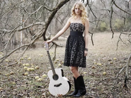 A music-themed HD wallpaper featuring a woman in a black lace dress standing beside a guitar, set against a natural, rustic background. Taylor Swift inspiration evident.