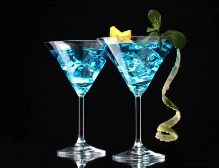 Two elegant blue cocktails with ice, garnished with a twist of lemon and mint, set against a dark background, creating a vibrant food and drink wallpaper for your HD desktop.
