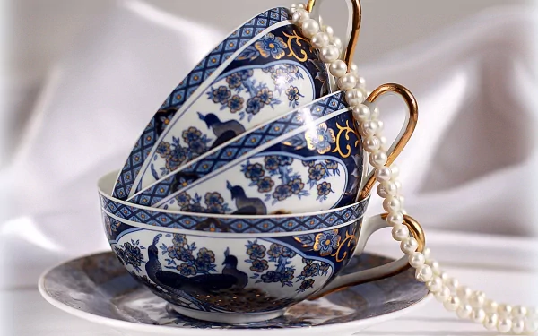 A still life 4K Ultra HD desktop wallpaper featuring elegant stacked blue and white patterned cups with a strand of pearls draped over them, captured in fine photography.