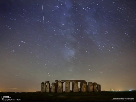 A stunning HD desktop wallpaper featuring Stonehenge set against a starry night sky, showcasing the ancient monument with celestial trails and a serene atmosphere.