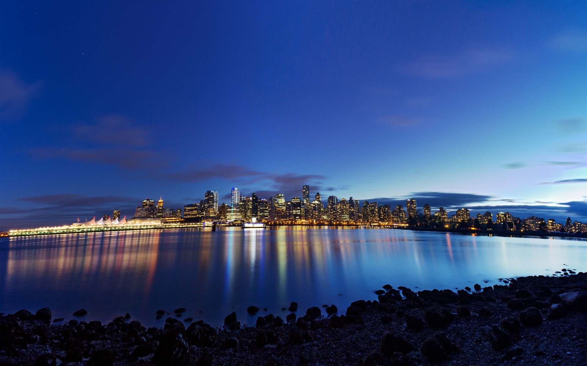 A stunning HD wallpaper featuring the Vancouver skyline at dusk, reflected in the calm waters, showcasing a blend of city lights and natural beauty.