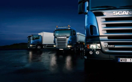 A striking HD wallpaper featuring Scania vehicles set against a twilight backdrop, showcasing three blue trucks with a gleaming surface on a reflective road.