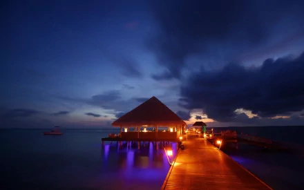 HD desktop wallpaper of a man-made pier glowing with warm lights extending into calm waters under a deep blue, cloudy evening sky.