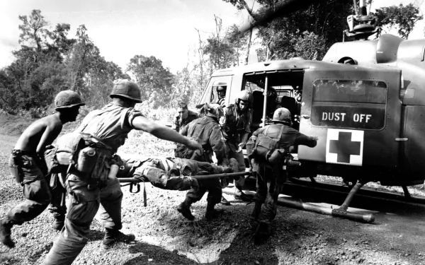 A black and white image depicting soldiers during the Vietnam War as they carry a stretcher toward a medical helicopter marked DUST OFF in a rugged jungle setting.