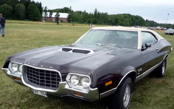 HD desktop wallpaper featuring a classic Ford Gran Torino Sport parked on a grassy field with trees and buildings in the background.