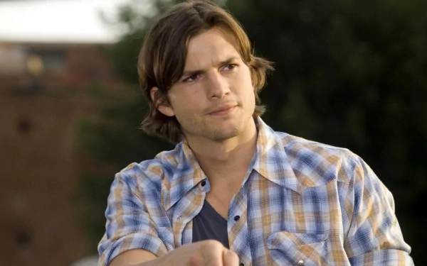 HD desktop wallpaper featuring celebrity Ashton Kutcher in a casual plaid shirt with a thoughtful expression against a blurred outdoor background.