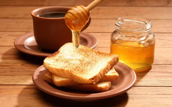 A cozy breakfast scene featuring toasted bread drizzled with honey, accompanied by a cup of coffee and a jar of honey, set on a rustic wooden table. HD wallpaper for food lovers.
