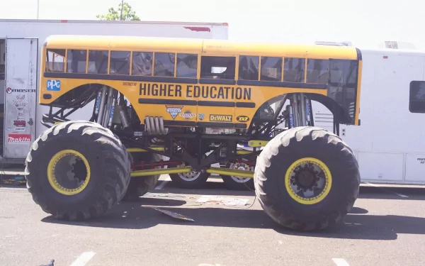 HD desktop wallpaper featuring a bright yellow bus modified into a monster truck with oversized tires, labeled HIGHER EDUCATION.