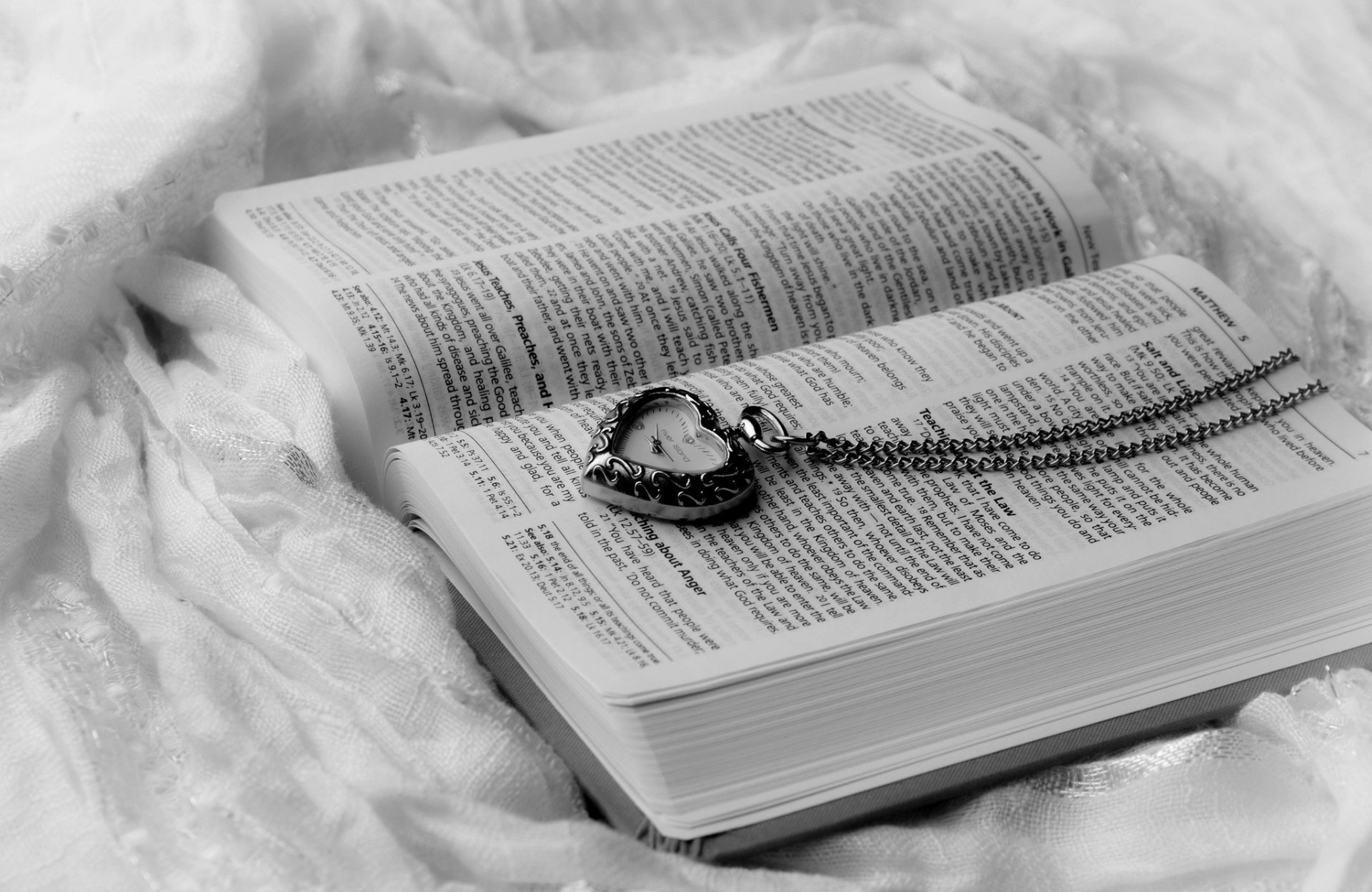 HD PC desktop wallpaper showing a man-made, heart-shaped pocket watch on a chain resting on the open pages of a book in a monochrome background.