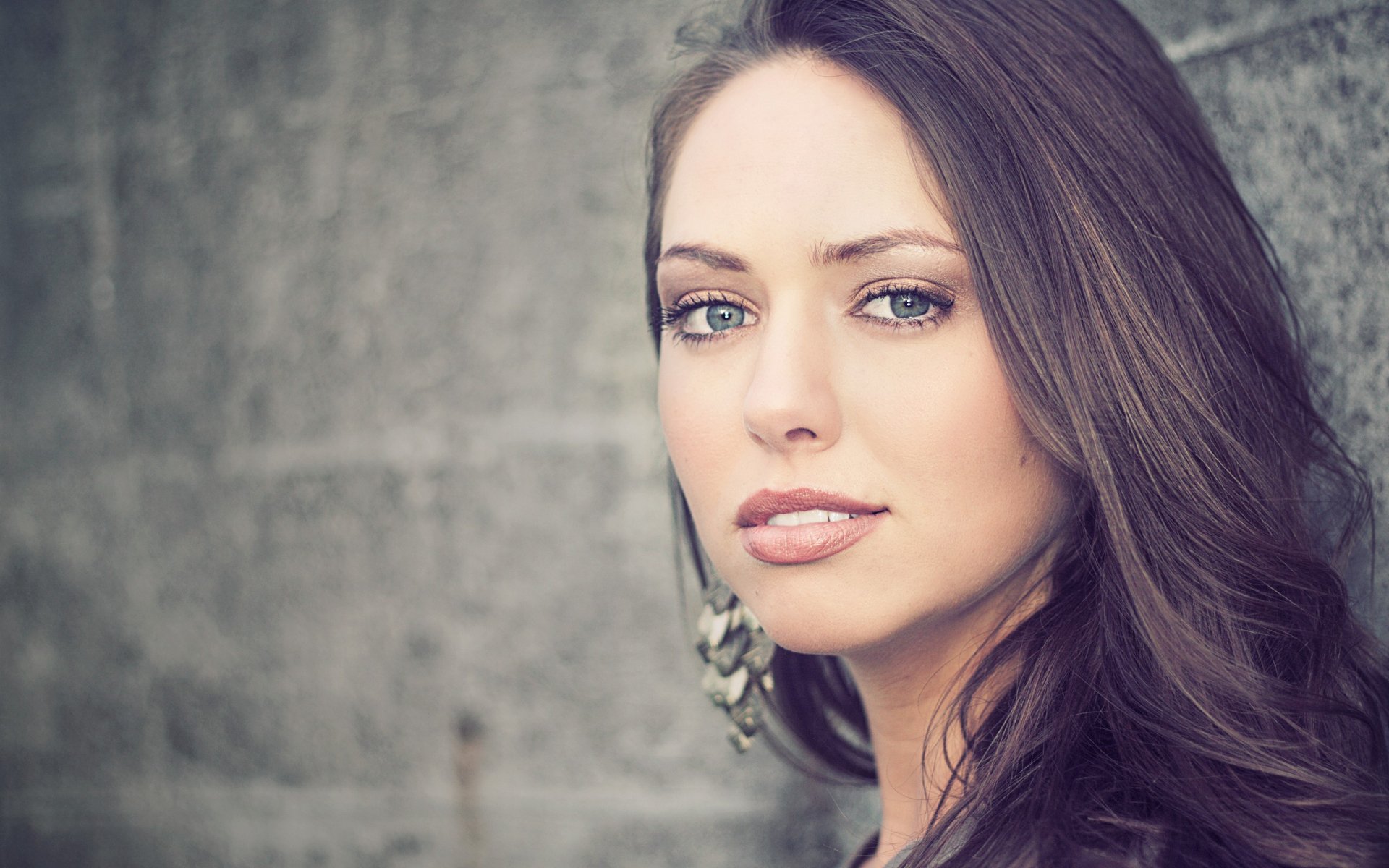 A close-up of a woman’s face with long, flowing hair and striking features, set against a textured background, suitable as an HD desktop wallpaper and background.