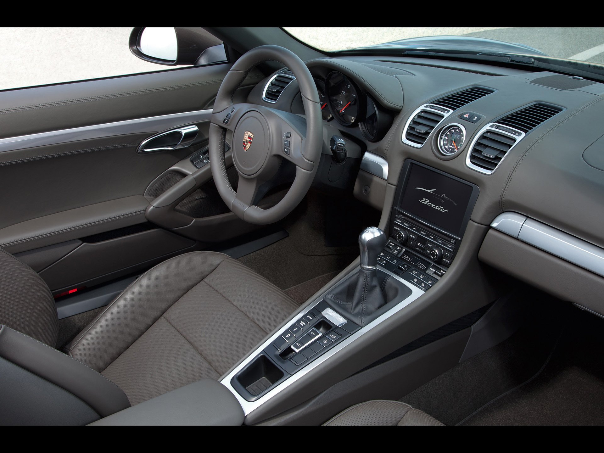 HD PC desktop wallpaper of a Porsche Boxster vehicle interior: driver-focused cockpit, leather seats, sporty steering wheel and center console with manual shifter.