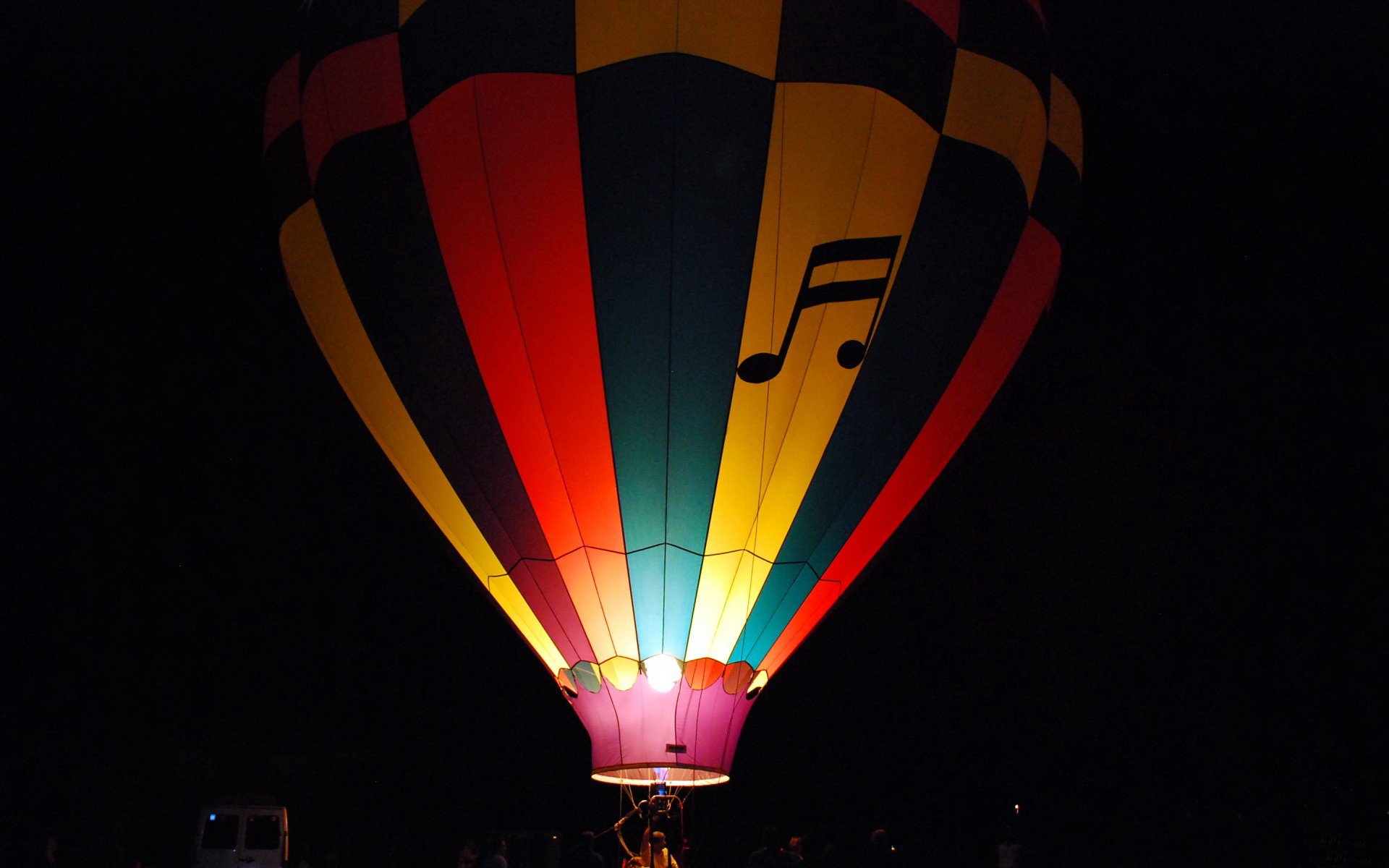 HD desktop wallpaper featuring a brightly lit hot air balloon with colorful stripes and a musical note against a dark night sky.