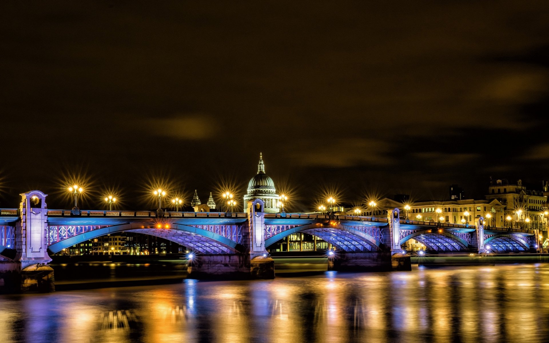 Night view of Southwark Bridge in London lit in blue, reflecting on the Thames — man-made structure captured as a 2K Quad HD PC desktop wallpaper and background.