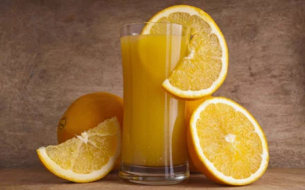 HD desktop wallpaper featuring a glass of orange juice surrounded by fresh orange slices against a rustic brown background.
