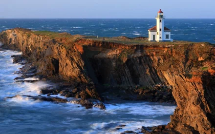 A stunning HD desktop wallpaper featuring a lighthouse perched on a rugged cliff, overlooking crashing waves and the vast ocean, showcasing the beauty of man-made structures against nature.