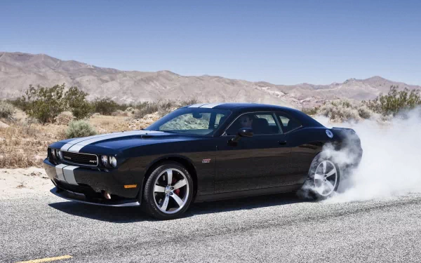 HD desktop wallpaper featuring a black Dodge Challenger performing a burnout on a desert road with mountains in the background.