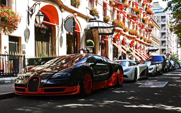 HD desktop wallpaper featuring a sleek black and orange Bugatti Veyron parked on a picturesque city street, lined with elegant buildings and vibrant flowers.