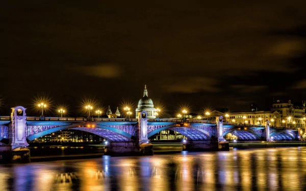 Night view of Southwark Bridge in London lit in blue, reflecting on the Thames — man-made structure captured as a 2K Quad HD PC desktop wallpaper and background.