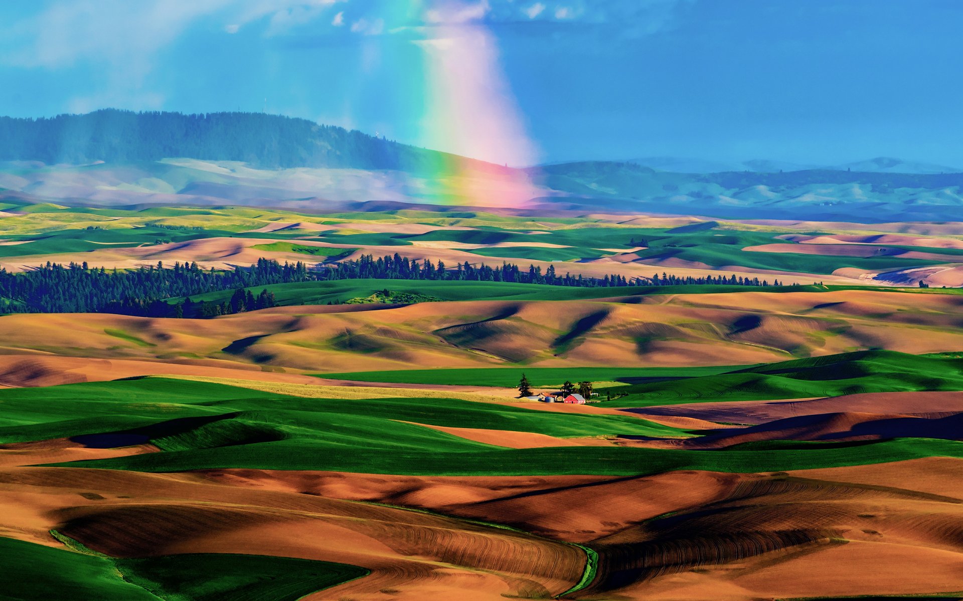 Vibrant landscape featuring rolling hills with green and brown fields under a clear blue sky, complemented by a rainbow, making it an eye-catching HD desktop wallpaper.