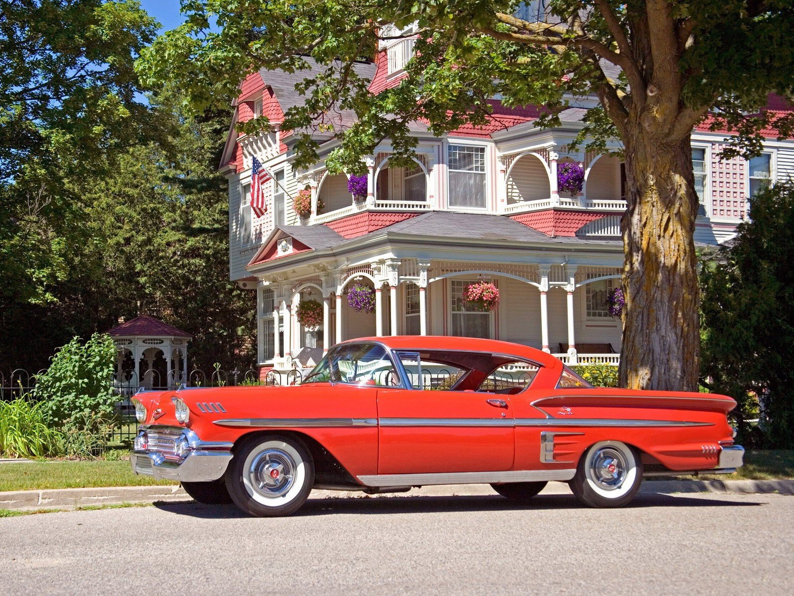 A vibrant red Chevrolet Impala parked in front of a classic Victorian-style house, captured in this HD PC desktop wallpaper and background.
