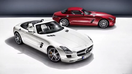 A striking white Mercedes-Benz SLS AMG convertible is showcased in the foreground, with a sleek red SLS AMG in the background, set against a clean, modern backdrop.