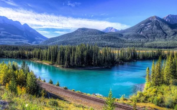 HD desktop wallpaper showcasing a vibrant river winding through lush forested mountains under a bright blue sky in a stunning nature landscape.