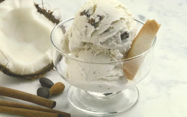 A delicious scoop of coconut ice cream is served in a clear glass bowl, accompanied by a slice of coconut and cinnamon sticks, creating a fresh and inviting food-themed HD desktop wallpaper.