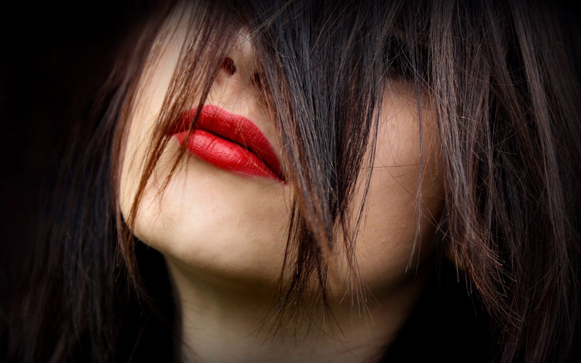 A close-up of a woman with dark hair partially covering her face, showcasing bold red lips. This HD desktop wallpaper captures a striking, intimate moment.