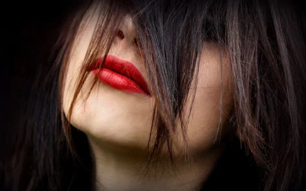 A close-up of a woman with dark hair partially covering her face, showcasing bold red lips. This HD desktop wallpaper captures a striking, intimate moment.