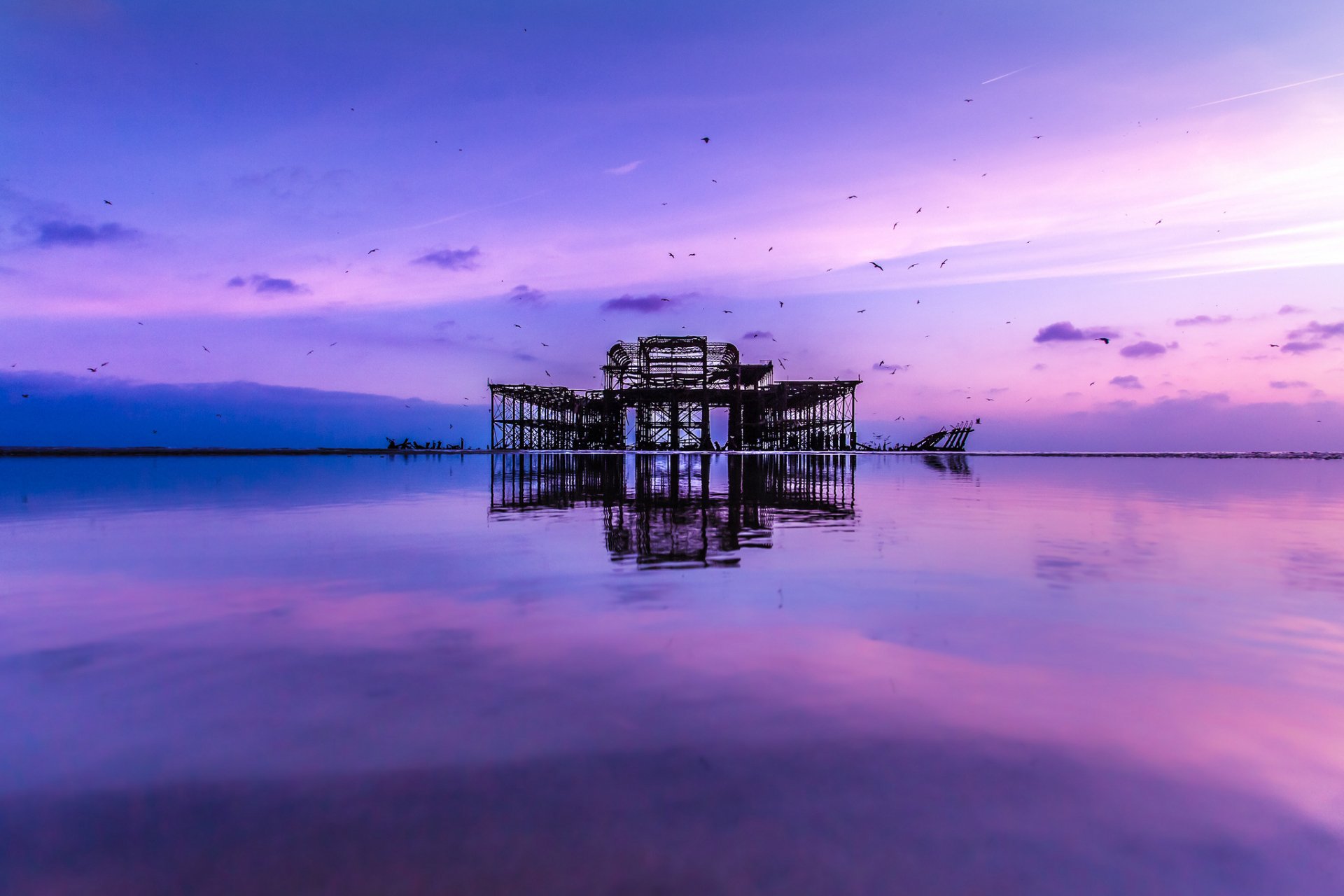 HD PC desktop wallpaper featuring a serene ocean scene at twilight with calm waters reflecting an old pier structure under a purple sky.