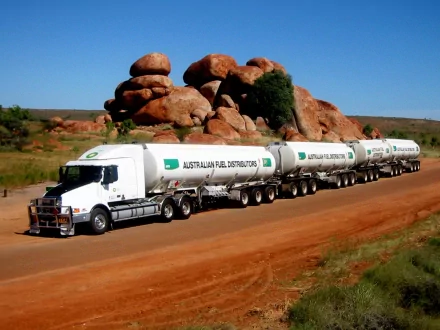 A Volvo road train hauling multiple fuel tankers on a red dirt road with rocky formations in the background, captured in HD for a desktop wallpaper.
