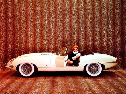 HD desktop wallpaper featuring a classic white Jaguar E-Type with a person seated inside, set against a textured, warm-toned background.