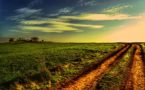 HD PC desktop wallpaper featuring a winding dirt path cutting through a vibrant green field under a dramatic sky at sunset.