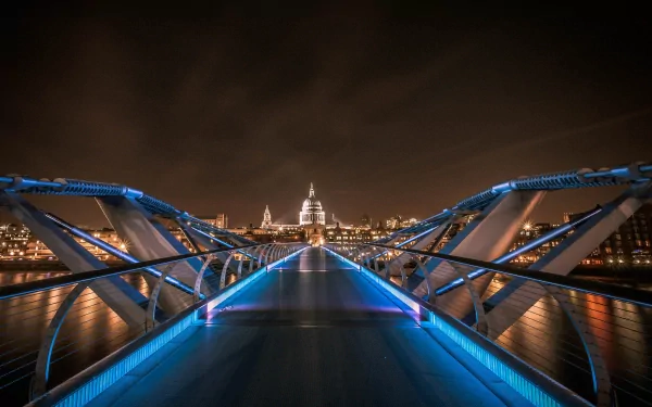 Night view of the illuminated Millennium Bridge in London, showcasing modern architecture with a clear path leading toward the city's skyline in this HD desktop wallpaper.