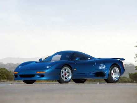 HD desktop wallpaper featuring a sleek blue Jaguar XJR sports car parked on a road with a scenic background.