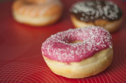 A vibrant pink doughnut topped with coconut flakes stands out against a red background, complemented by other doughnuts in various flavors. A delicious food-themed 4K Ultra HD wallpaper.